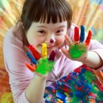 Young girl with down syndrome showing her multi colored painted hands.